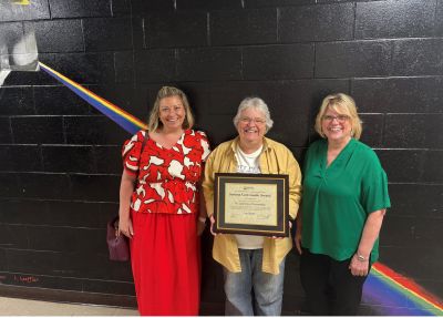 Three ladies smiling while one holds certificate