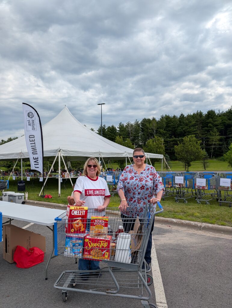 Two volunteers pose standing behind food at table.