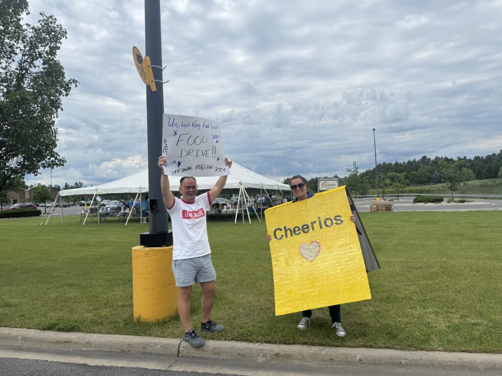 Volunteer holds "Food Drive" sign next to woman dressed in Cheerios cereal box.