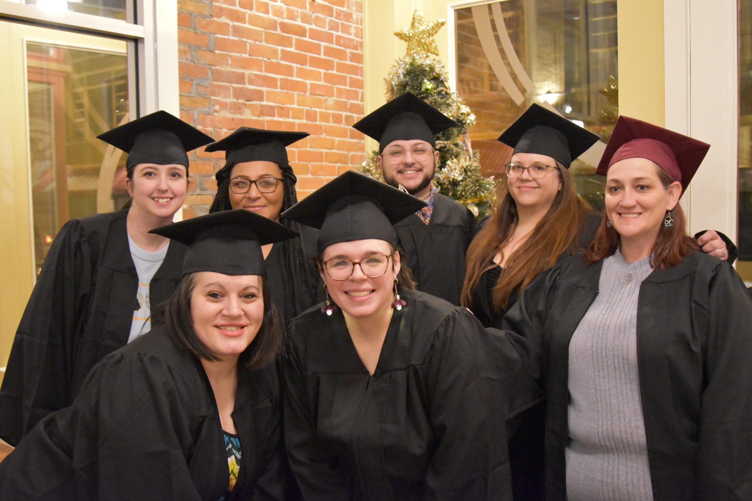 A group of seven adult graduates pose with black caps and gowns.