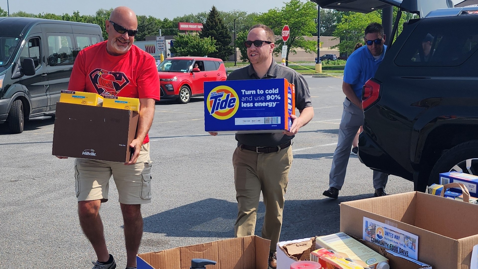 Two men carrying boxes of food while another unloads a trunk