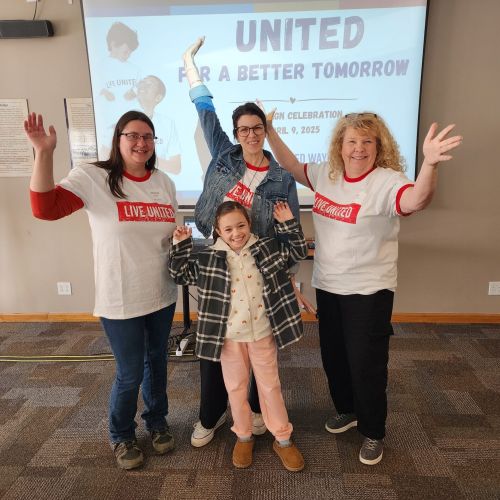 Small group of people wearing LIVE UNITED shirts, raising their arms in joy