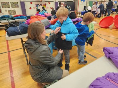 Woman kneels down and helps child try on a coat