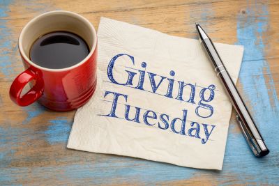 Coffee cup and pen next to napkin imprinted with "Giving Tuesday"