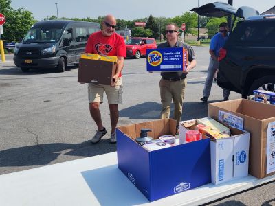 Ryan Piche and volunteer carry donations from a car to a table at the food drive