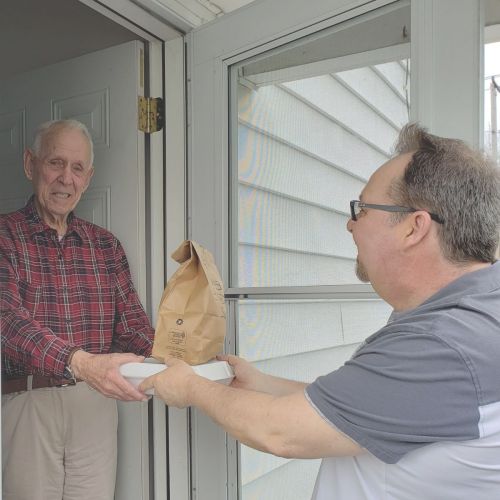 man handing an older man a box and bag of food