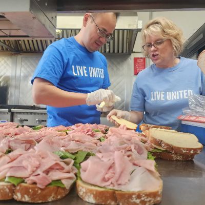 people in live united shirts making lots of cold cut sandwitches