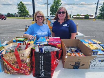 Two women leaders of United Way and Food Bank of CNY smiling with food donations